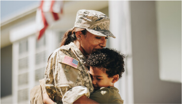 Veteran hugs child outside of a home purchased using a VA loan.