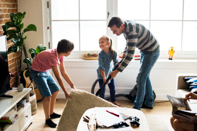 Family works together on their spring cleaning checklist by vacuuming living room.