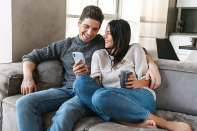 Couple sitting together on couch researches a cash-out refinance loan on their cell phone.