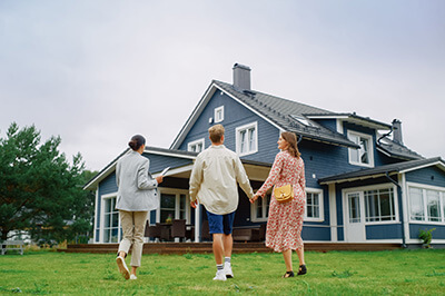 Real estate agent showing a beautiful big house to a young successful couple. People standing outside on a warm day on a lawn, talking with business woman, discussing buying a new home.