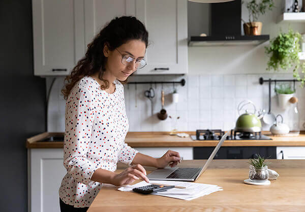 A homeowner at a kitchen island on a laptop researching income calculation for the home loan process